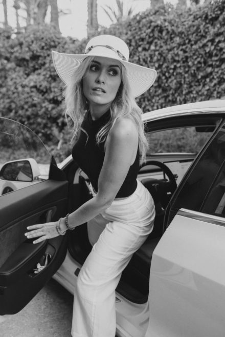 Black and white photograph of a woman getting out of a car wearing a big hat