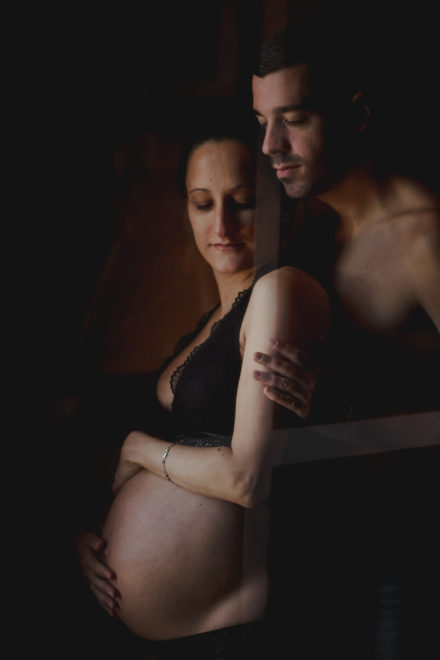 Artistic photograph of the couple embracing shirtless looking at the woman's belly.