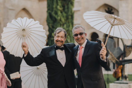 Two smiling wedding guests holding their white parasols.