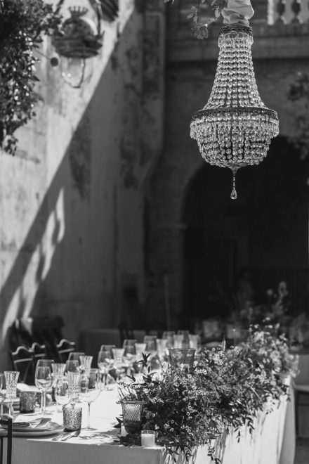 Black and white photograph of the banquet table with all the tableware set and a large crystal chandelier on top.