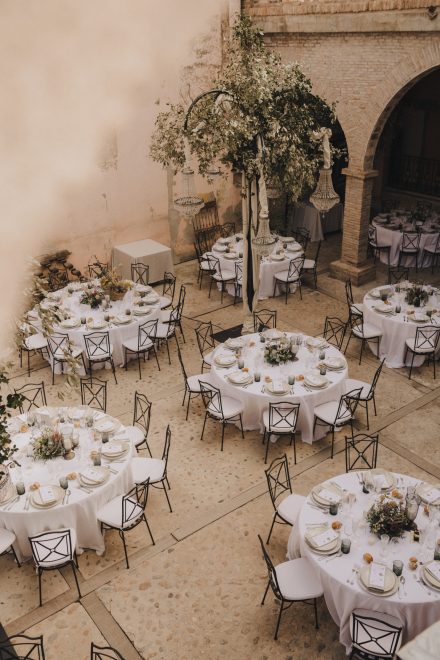 Photograph from upstairs of the banquet area showing several round tables with chairs and white tablecloths in a church courtyard.