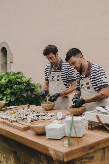 Photograph of two catering staff members preparing clams for guests.