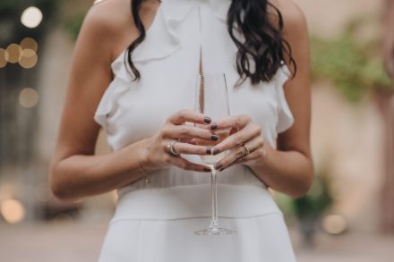 Shoulder to waist photograph of the bride holding a glass of champagne with both hands showing her engagement and wedding rings.