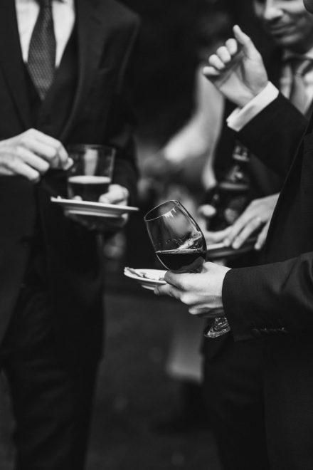 Black and white photograph of two guests each holding a glass of wine and a plate of appetizers.