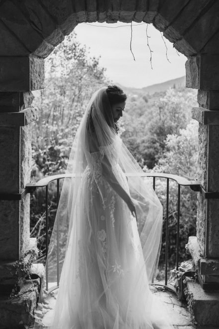 Black and white photograph of the bride posing on a balcony of the church where a large forest can be seen in the background.
