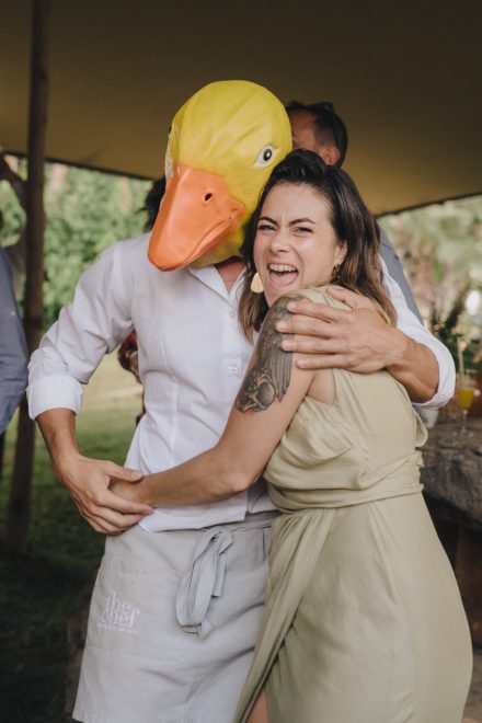 Photograph of a man with a yellow chick mask and orange beak hugging a woman.