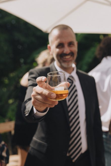 Photograph of a man raising a glass of alcohol to the camera as a toast.