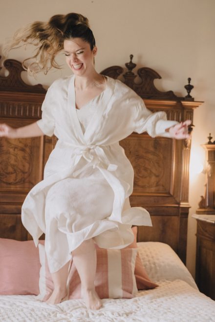 Photograph of bride in gown jumping on the bed