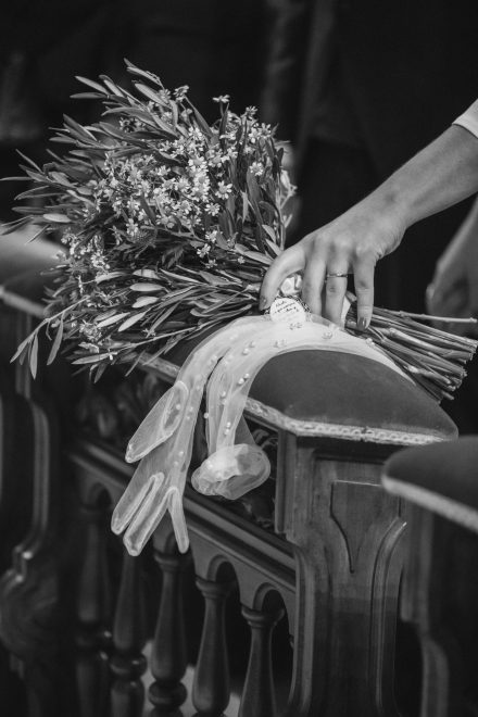 Close-up photograph of the bride's hand resting the bouquet of flowers on the church pew