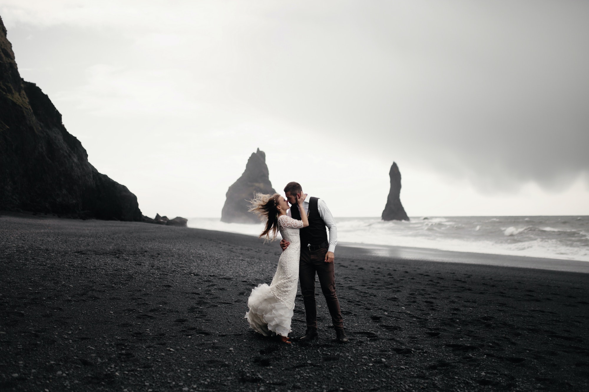 Couple in wedding dresses kissing on a beach on a windy day.