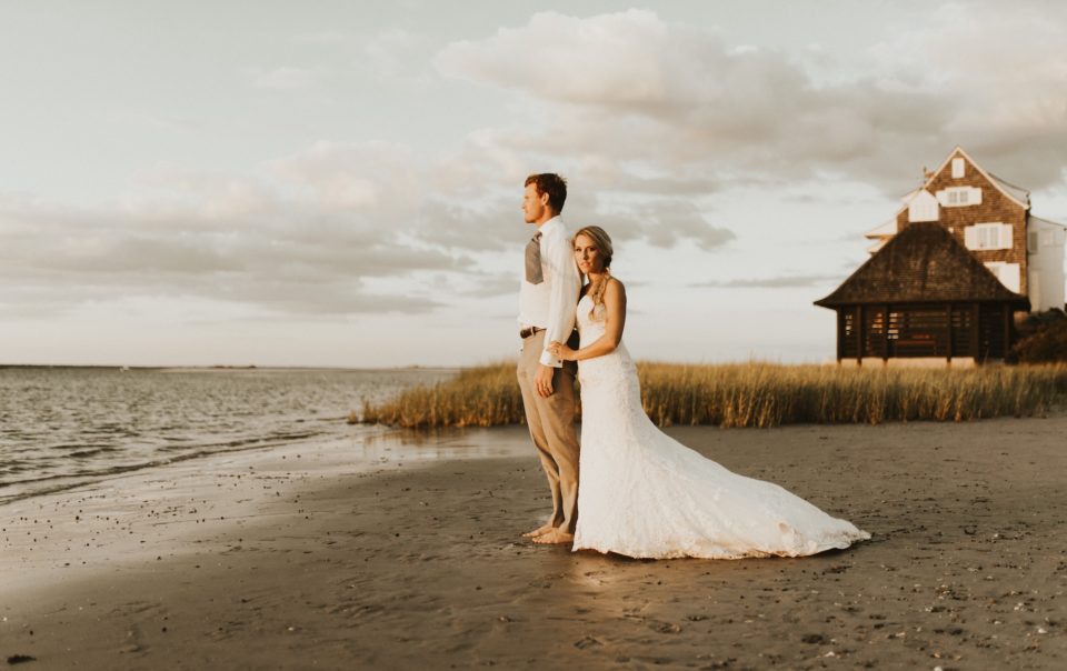 engaged couple on a beach with a bungalow behind them
