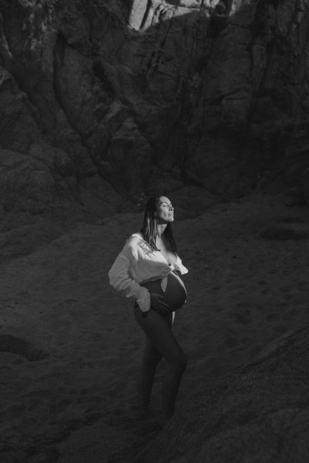 Black and white photograph of Ale on the sand of the beach caressing her belly