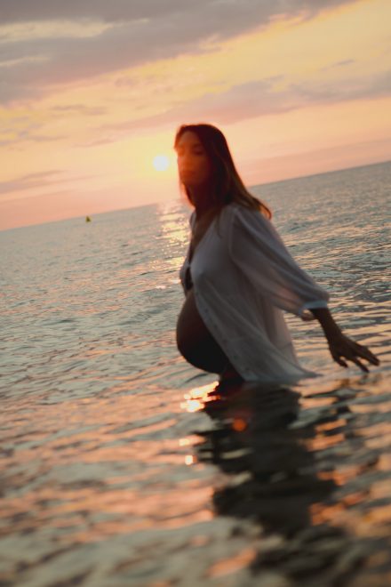 Pregnancy photo of Ale on the seashore with an open shirt exposing her belly.
