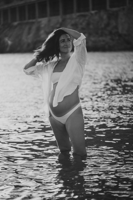 Black and white pregnancy photo of Helena on the seashore with an open shirt exposing her belly.