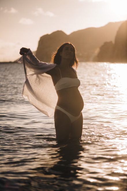 Pregnancy photo of Helena on the seashore with an open shirt exposing her belly.