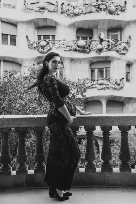 Black and white photograph of Marcelina, on a balcony in a see-through dress, caressing her belly.