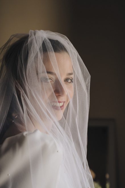 Photograph of the bride with her face covered behind the veil looking at the camera.